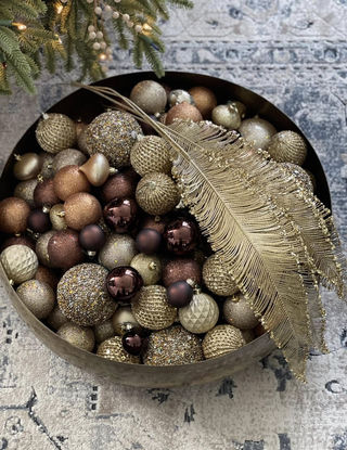 Gold holiday ornaments in metal bowl with feather