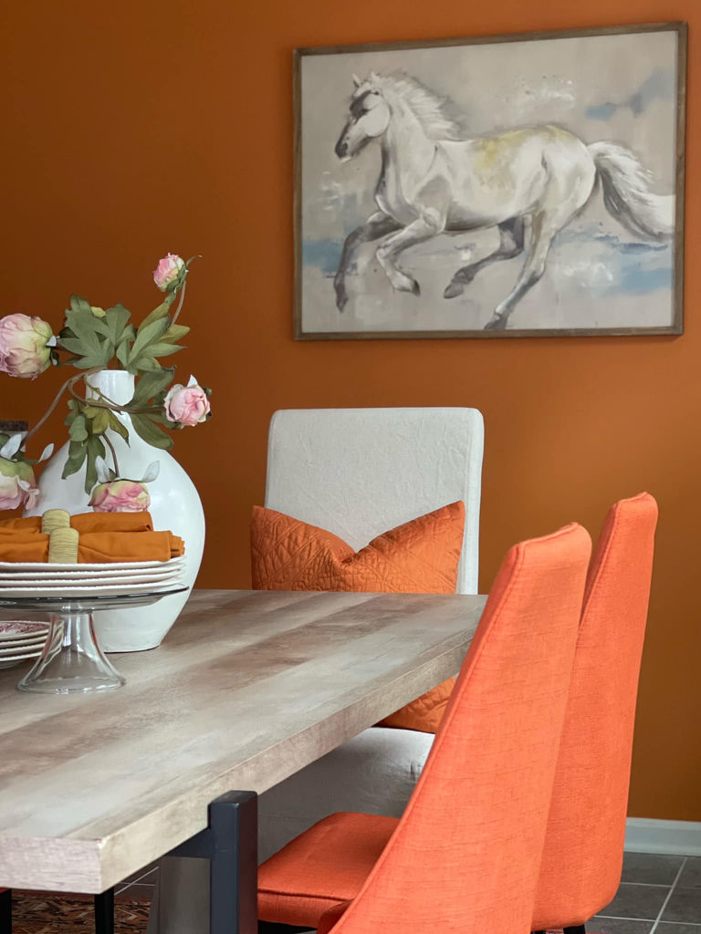 Boldly styled dining room with orange accent wall and horse art — Cosmopolitan Interiors decor styling