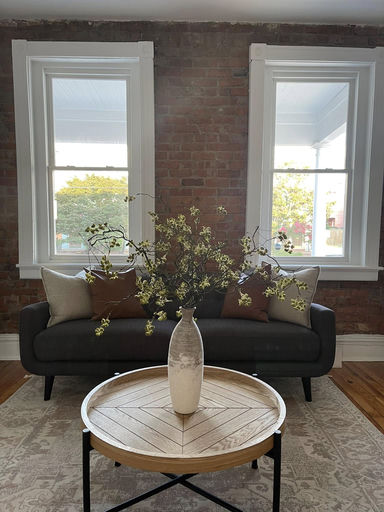 Beautifully staged living room with exposed brick wall, dark sofa and herringbone wood coffee table — Cosmopolitan Interiors Richmond
